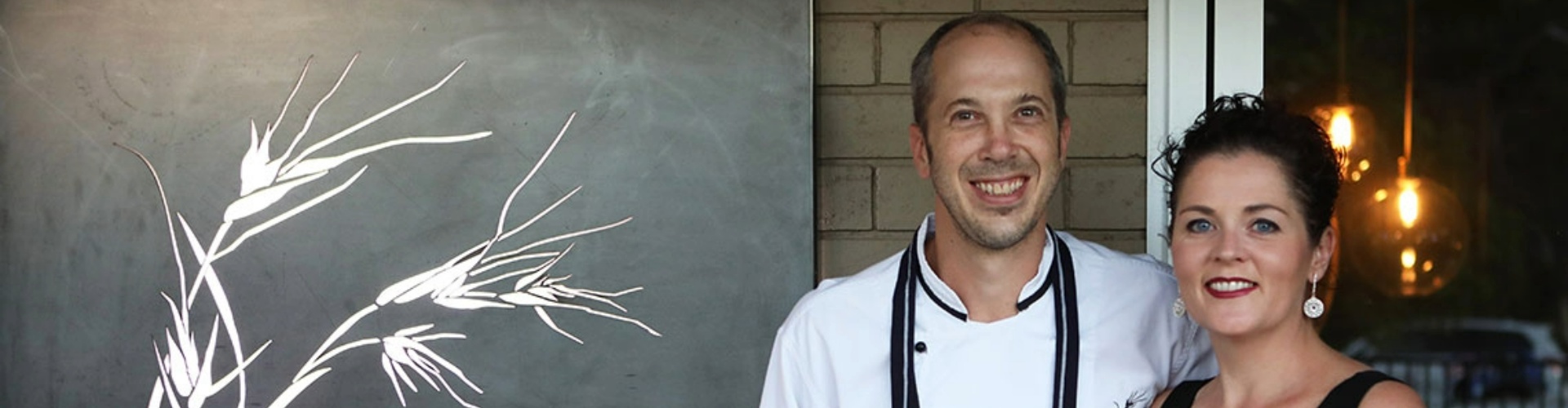 Brad and Natalie from Veldt Restaurant in Dubbo standing together and smiling next to their restaurant logo.