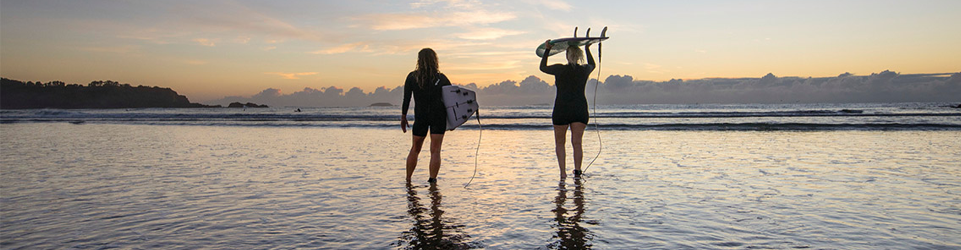 surfers look out to sea standing in water on Coffs Harbour beach