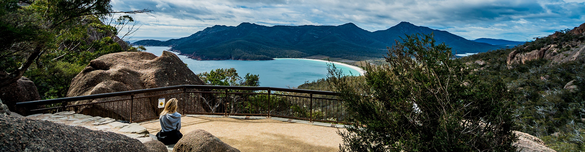A woman sitting on a rock, taking in the view of Wineglass Bay from Wineglass Bay Track Lookout