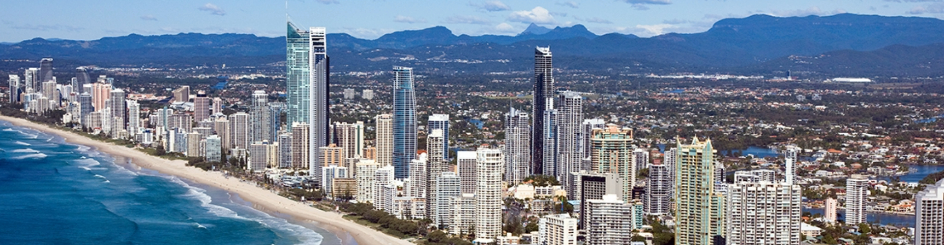 gold-coast-panorama-qld-1920x500 A panoramic view of Gold Coast beach and city skyline, with mountains on the horizon.