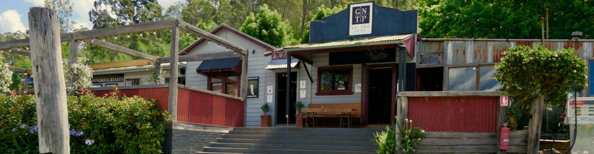 great-northern-trading-post-1920x500 Stairs leading up to a low-set cafe and patio surrounded by trees on a sunny day.