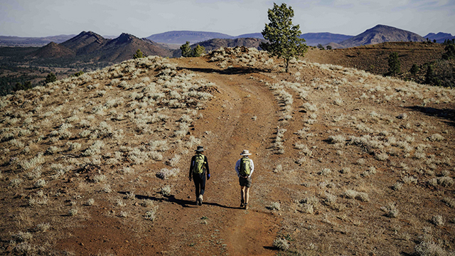 Two people hiking on a red dirt track