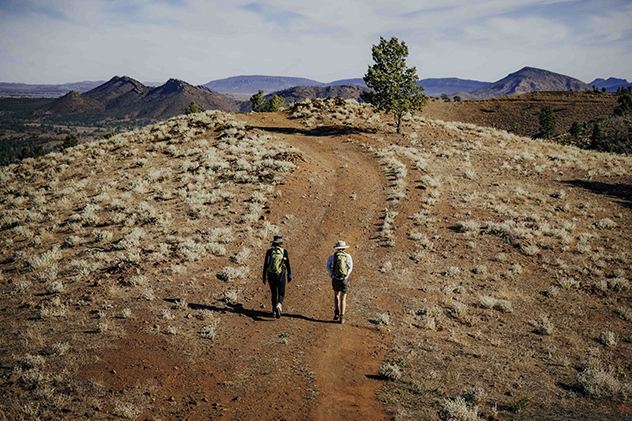Two people hiking on a red dirt track
