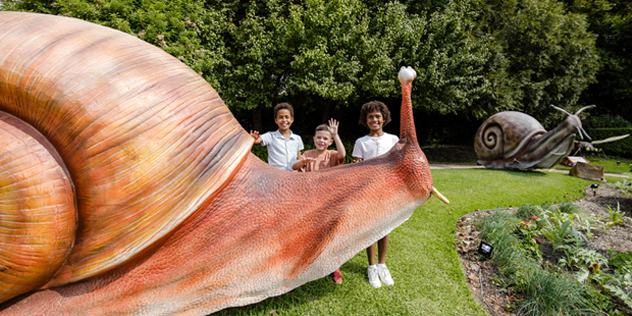 A huge snail statue with two children standing behind it