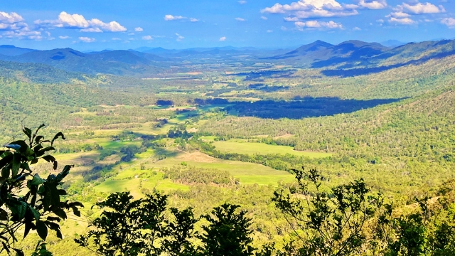 view down into valley with paddocks and tree-covered slopes on a sunny day