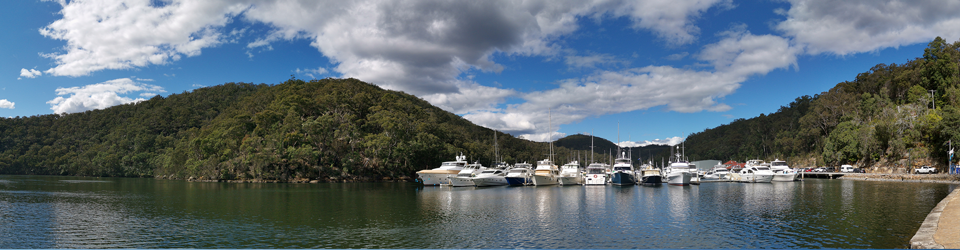 Beautiful panoramic view of a river with reflections of blue sky, boats, mountains and trees, Bobbin Head, Ku-ring-gai Chase National Park