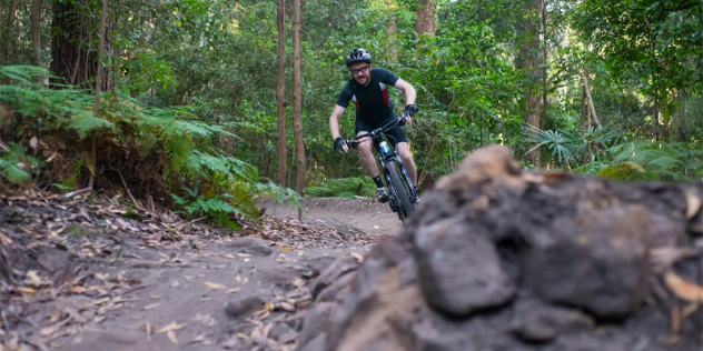 A man mountain biking down a hillside path in a forest.