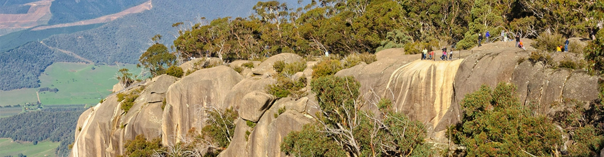 mount-buffalot-bright-vic-1920x500 The top of a mountain high above green fields below, covered with rounded rocks and trees.