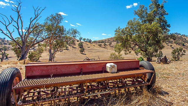 faded red farming equipment on dry grassland with hills and trees in the background