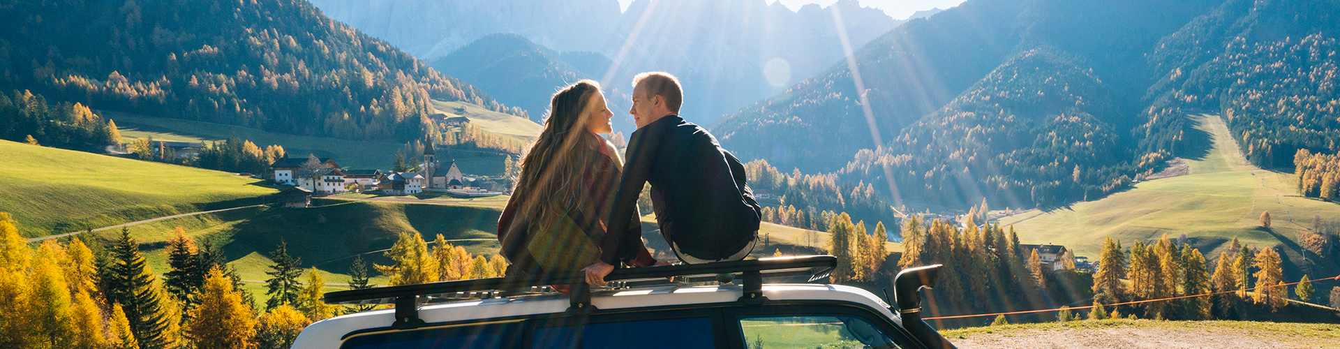 TitleCouple sit on car rooftop looking at mountains in the distance