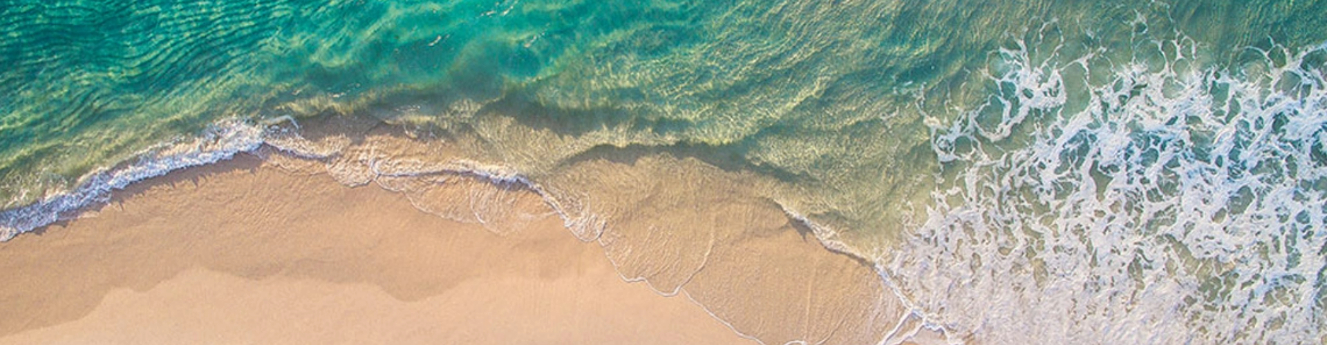 sand-and-ocean-only-1920x500 Aerial view of a turquoise blue and foamy wave washing over sand, nothing else.