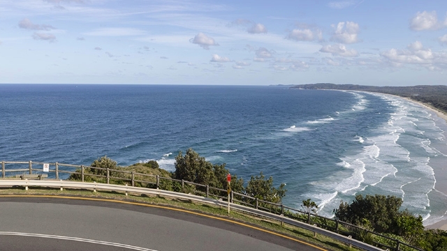 Sydney to Gold Coast curve in the road overlooks waves crashing on a beach