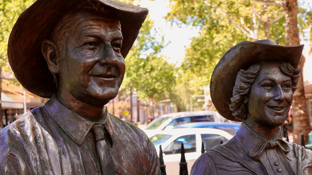 head and shoulders of life-size bronze monument of slim dusty and joy mckeen with cars and streetscape behind