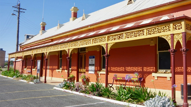 A bright orange brick train station on a sunny day, with yellow Victorian trim around poles along the front.