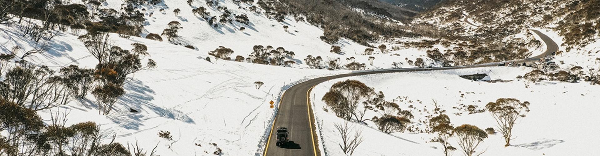 Thredbo Snowy Mountains Kosciuszko National Park NSW four wheel drive vehicle drives along a road that winds through a snowy mountainous landscape