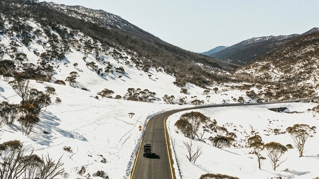four wheel drive vehicle drives along a road that winds through a snowy mountainous landscape