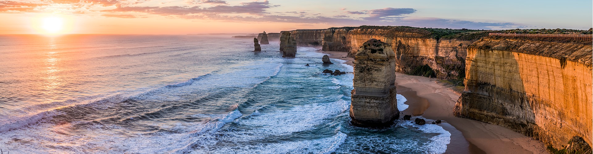 twelve-apostles-at-golden-hour-1920x500 Panoramic view of a warm orange sunset over the ocean and twelve apostles rock formations in Victoria State.