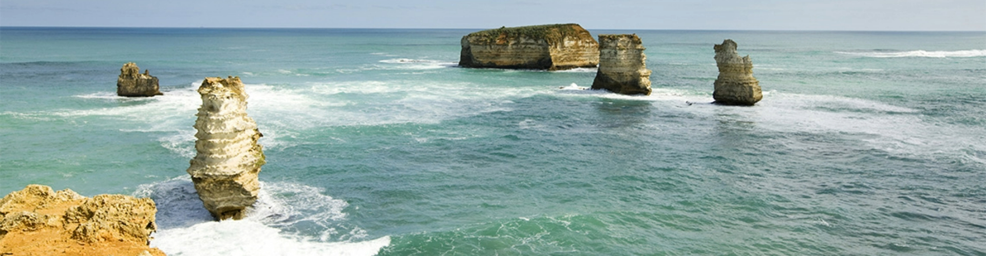 twelve-apostles-cliff-view-1920x500 View from the cliffs along Great Ocean Road out at four of the Twelve Apostle rock formations in the sea below.