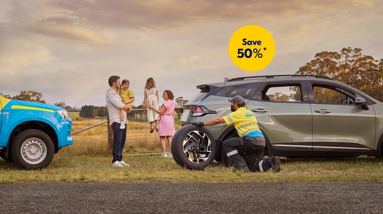 NRMA Roadside assistance staff member helping to replace tyre for vehicle on the side of the road while family of four look on