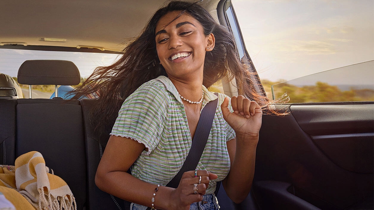 Girl sitting in the back seat of a moving car, seatbelt on, hair blowing in the wind, grooving to music with hands raised