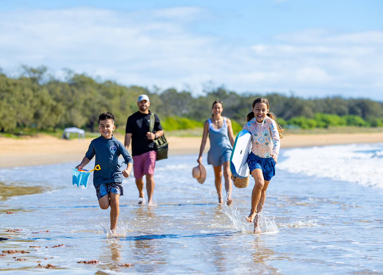 A family of four joyfully walking and running along the shoreline, ready for a fun-filled day in the sun and surf