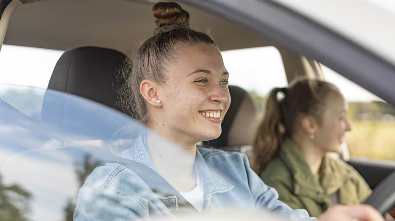 Two girls beaming with smiles while driving, sharing a fun and carefree moment on the road