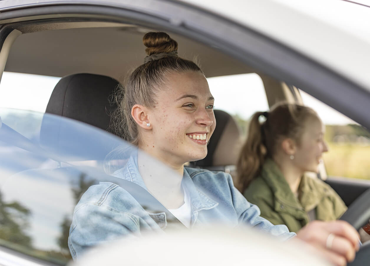 Two girls beaming with smiles while driving, sharing a fun and carefree moment on the road