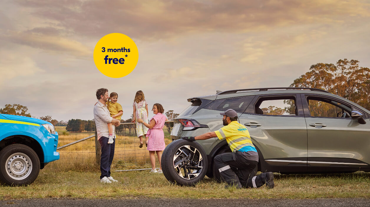 NRMA Roadside assistance staff member helping to replace tyre for vehicle on the side of the road while family of four look on