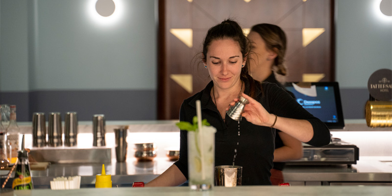 female bartender pouring liquid into a cocktail shaker