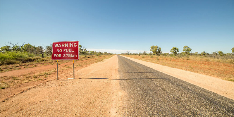 red warning sign that says no fuel for 375 kilometres on a dusty outback road