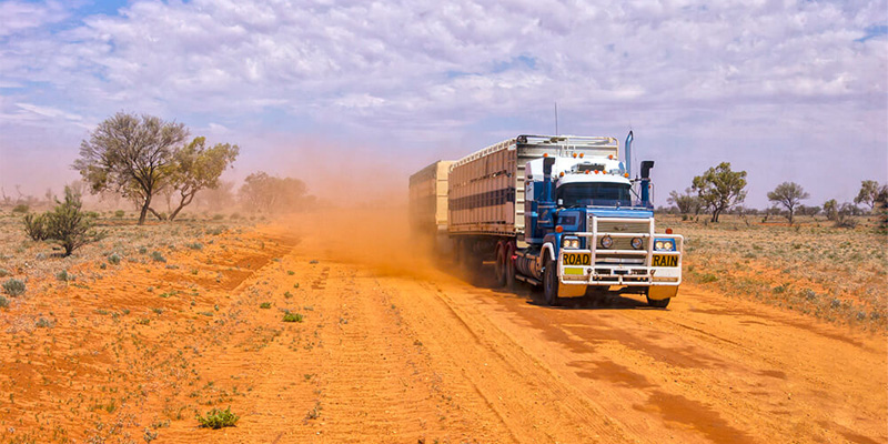 blue freight truck driving down a dusty orange road